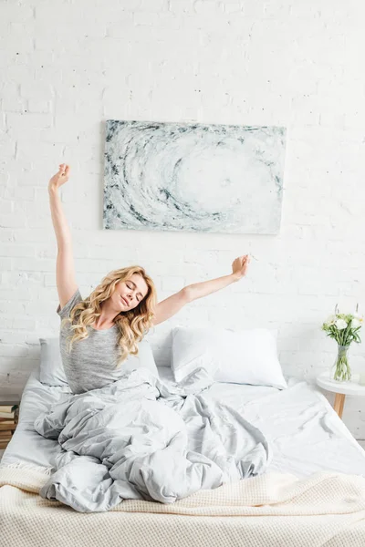 Happy young woman sitting with outstretched hands while waking up at home — Stock Photo