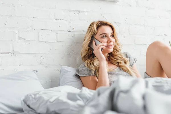 Селективное внимание счастливой девушки, говорящей на смартфоне в постели — стоковое фото