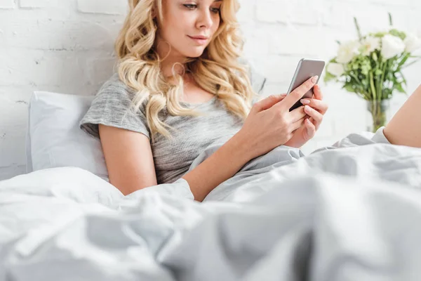 Selective focus of beautiful girl using smartphone in bed — Stock Photo