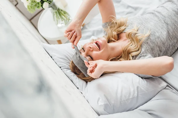 Selective focus of cheerful girl touching sleeping mask in bedroom — Stock Photo