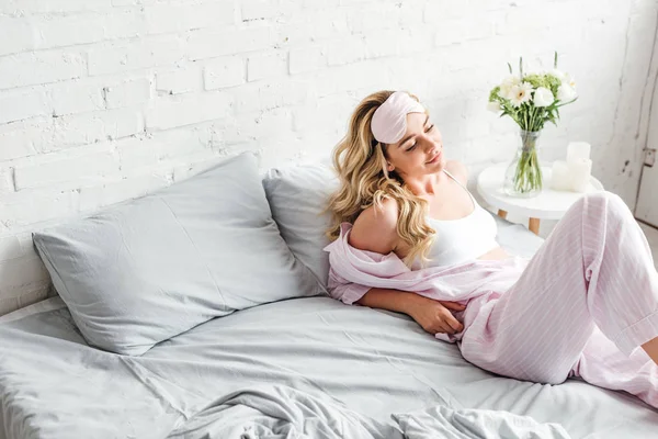 Молода жінка з маскою для очей відпочиває на ліжку вдома — стокове фото