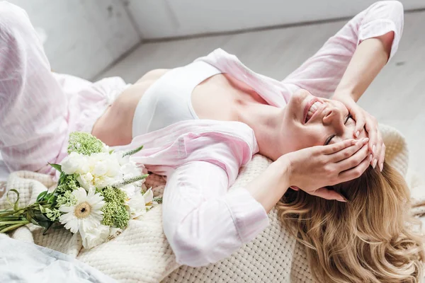 Enfoque selectivo de la mujer joven positiva acostada cerca de flores en la cama - foto de stock