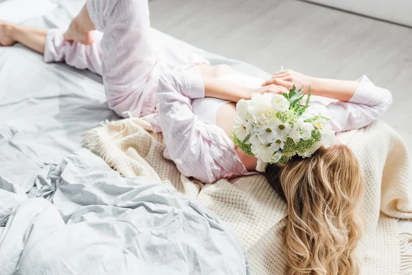 Jovem mulher cobrindo rosto com flores enquanto deitado na cama — Fotografia de Stock