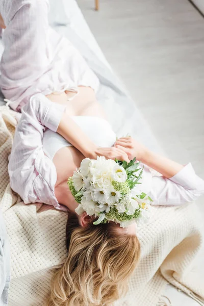 Girl covering face with flowers while lying on bed — Stock Photo