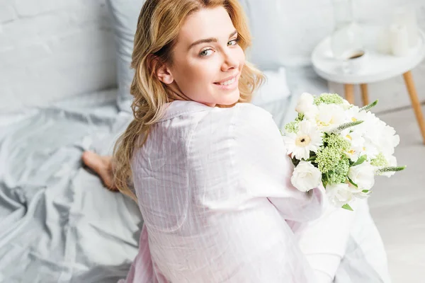 Вибірковий фокус красивої жінки, що сидить на ліжку з квітами — стокове фото