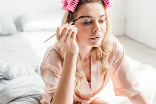 Belle femme en boucles de cheveux roses coiffant les sourcils dans la chambre — Photo de stock