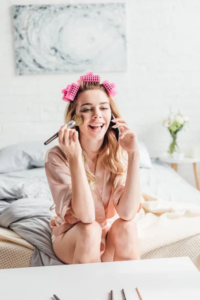 Chica feliz sosteniendo cepillo cosmético mientras habla en el teléfono inteligente - foto de stock