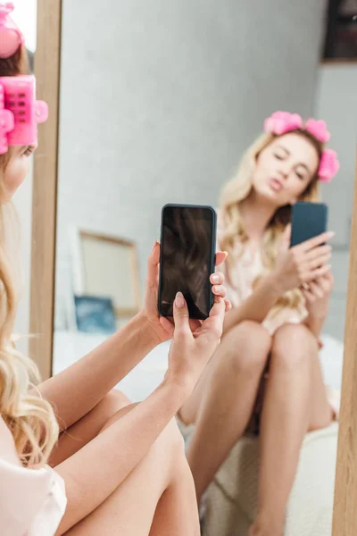Selective focus of woman with duck face holding smartphone while taking photo near mirror — Stock Photo