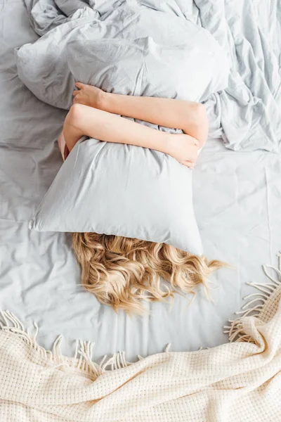 Vista superior da mulher cobrindo rosto com travesseiro no quarto — Fotografia de Stock