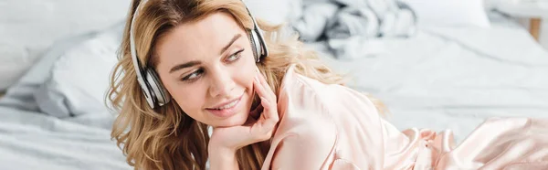 Panoramic shot of cheerful girl in headphones listening music in bedroom — Stock Photo