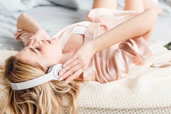 Вибірковий фокус дівчина торкається навушників під час прослуховування музики в спальні — стокове фото