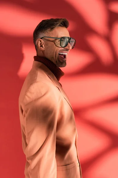 Uomo felice ed elegante in occhiali da sole su rosso con ombre — Foto stock