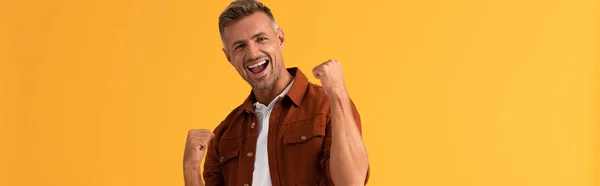 Panoramic shot of excited man with clenched fists isolated on orange — Stock Photo