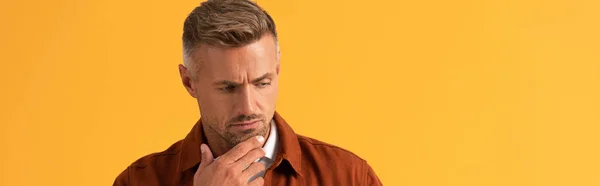Tiro panorâmico de belo homem tocando rosto enquanto pensava isolado em laranja — Fotografia de Stock