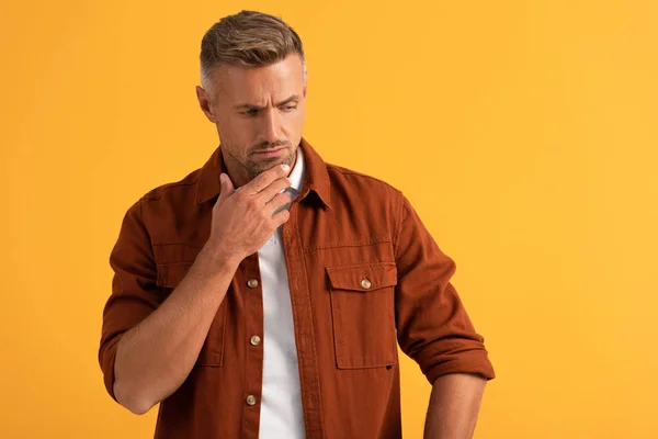 Hombre guapo tocando la cara mientras piensa aislado en naranja - foto de stock