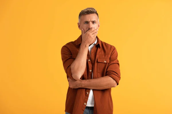 Hombre molesto cubriendo la boca y mirando a la cámara aislada en naranja - foto de stock