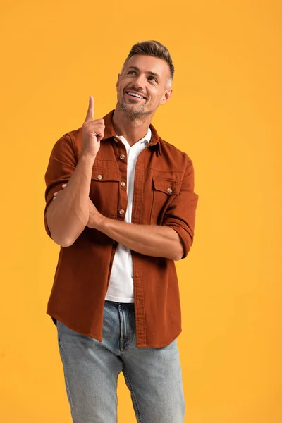 Hombre alegre señalando con el dedo y mirando hacia arriba aislado en naranja - foto de stock