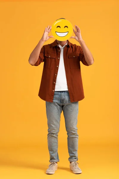 KYIV, UKRAINE - SEPTEMBER 24, 2019: man covering face with happy emoticon on orange — Stock Photo
