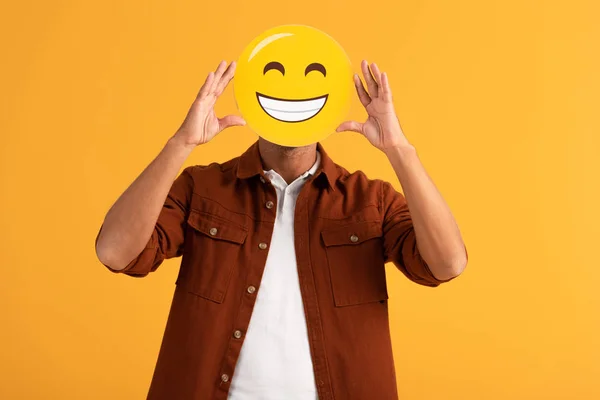 KYIV, UCRANIA - 24 DE SEPTIEMBRE DE 2019: hombre cubriendo la cara con emoticonos felices aislados en naranja - foto de stock