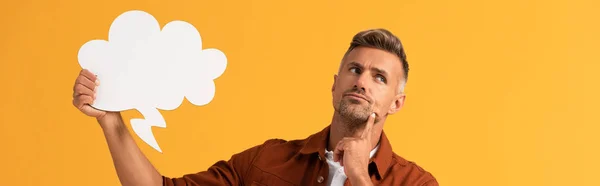 Panoramic shot of pensive man holding black thought bubble isolated on orange — Stock Photo