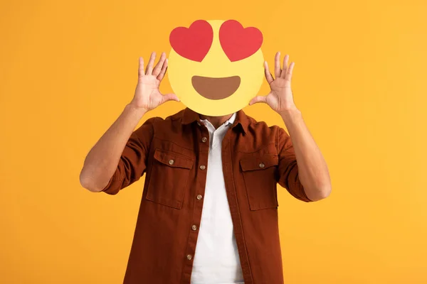 QUIIV, UCRÂNIA - SETEMBRO 24, 2019: homem cobrindo rosto com olhos de coração emoticon desenhos animados isolado em laranja — Fotografia de Stock