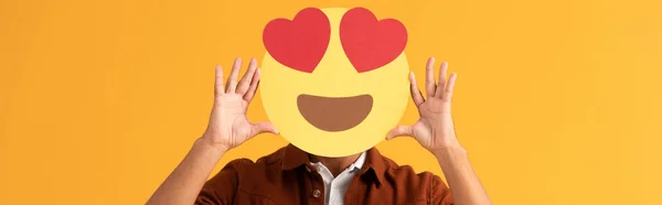 QUIIV, UCRÂNIA - SETEMBRO 24, 2019: tiro panorâmico do homem cobrindo rosto com olhos de coração emoticon desenhos animados isolado em laranja — Fotografia de Stock