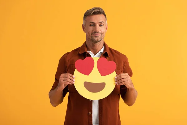 KYIV, UCRANIA - 24 DE SEPTIEMBRE DE 2019: Hombre guapo sosteniendo ojos de corazón emoticono de dibujos animados aislado en naranja - foto de stock