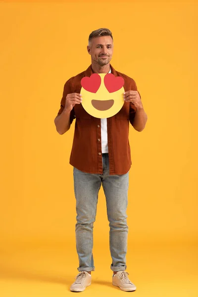 KYIV, UKRAINE - SEPTEMBER 24, 2019: handsome man holding heart eyes cartoon emoticon on orange — Stock Photo