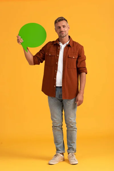 Hombre feliz sosteniendo burbuja de habla verde en naranja - foto de stock