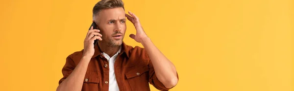 Panoramic shot of emotional man gesturing while talking on smartphone isolated on orange — Stock Photo