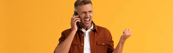 Plano panorámico del hombre enojado gritando mientras habla en el teléfono inteligente aislado en naranja - foto de stock