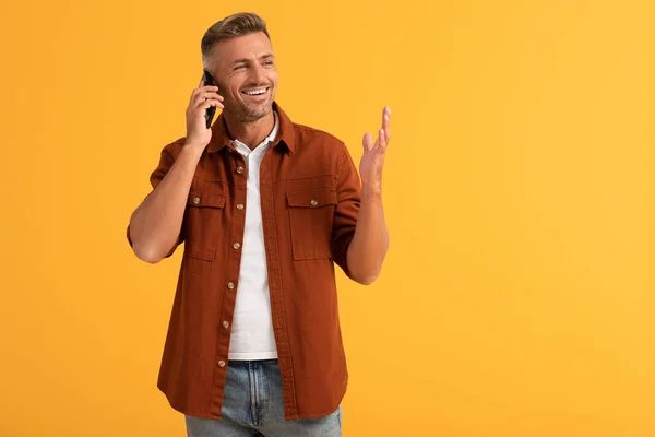 Hombre feliz gesto y hablar en el teléfono inteligente aislado en naranja - foto de stock