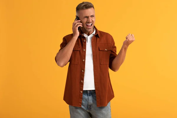 Angry man screaming while talking on smartphone isolated on orange — Stock Photo