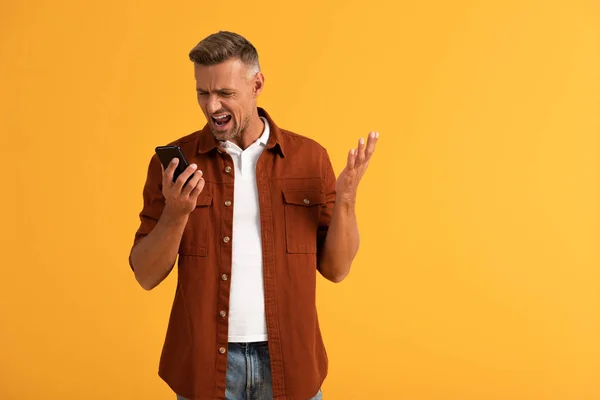 Hombre enojado gritando mientras sostiene teléfono inteligente aislado en naranja - foto de stock