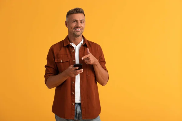 Homem feliz apontando com o dedo para smartphone isolado em laranja — Fotografia de Stock