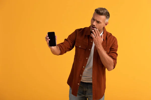 Hombre sorprendido sosteniendo teléfono inteligente con pantalla en blanco aislado en naranja - foto de stock