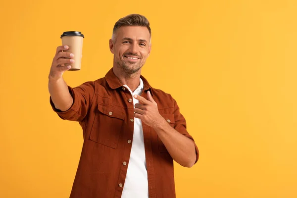 Homme joyeux pointant du doigt à tasse en papier isolé sur orange — Photo de stock