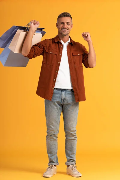 Cheerful man holding colorful shopping bags on orange — Stock Photo