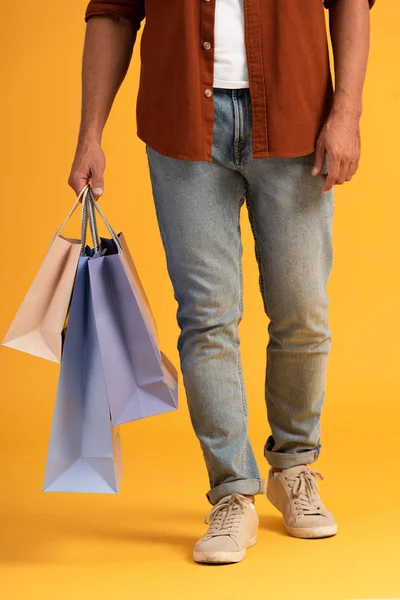 Cropped view of man standing with shopping bags on orange — Stock Photo