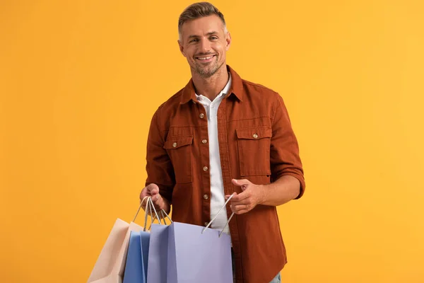 Hombre feliz sosteniendo bolsas aisladas en naranja - foto de stock