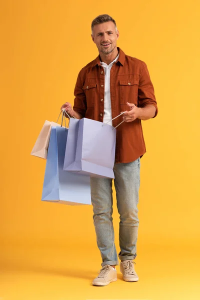 Hombre feliz sosteniendo bolsas de compras mientras está de pie en naranja - foto de stock