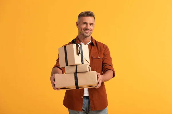 Hombre feliz sosteniendo regalos aislados en naranja - foto de stock