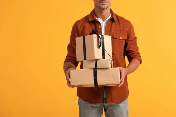 Vista recortada de hombre feliz sosteniendo regalos aislados en naranja - foto de stock