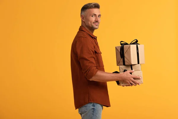 Cheerful man holding presents isolated on orange — Stock Photo