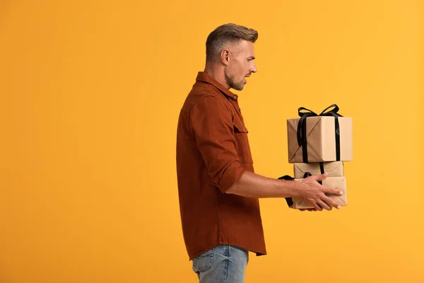 Vista lateral del hombre sorprendido sosteniendo regalos aislados en naranja - foto de stock
