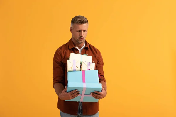 Handsome man looking at gift boxes isolated on orange — Stock Photo