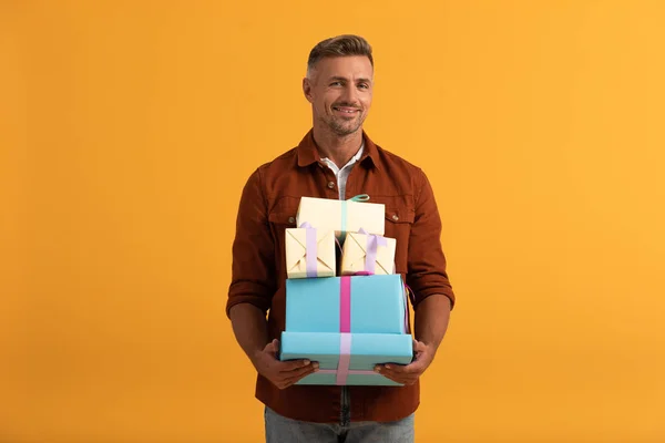 Hombre guapo sonriendo mientras sostiene cajas de regalo aisladas en naranja - foto de stock