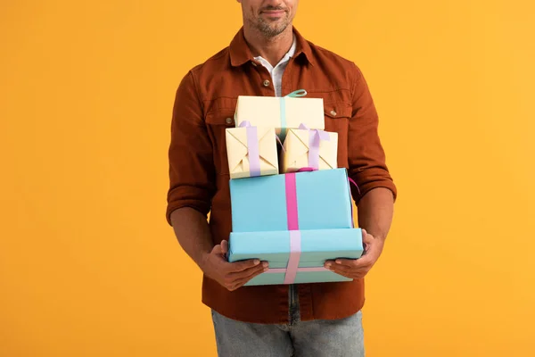Vista recortada del hombre sonriendo mientras sostiene cajas de regalo aisladas en naranja - foto de stock