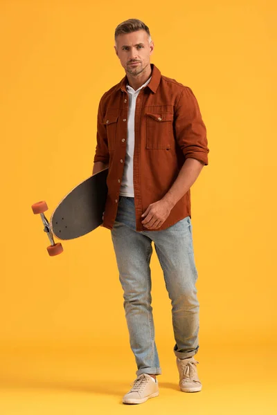 Hombre guapo de pie y la celebración de penny board en naranja - foto de stock