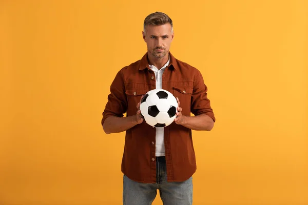 Hombre serio sosteniendo fútbol aislado en naranja - foto de stock